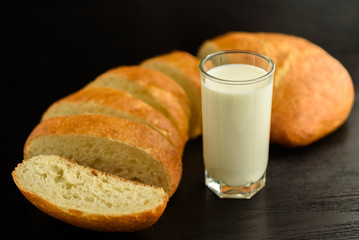 Ciabatta and a glass of milk on a wooden background.
