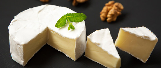 Cheese camembert or brie with walnuts on black background, side view. Close-up.
