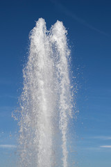 Water jet from a vertical fountain cut out against a blue sky.