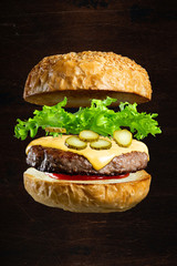 Floating burger isolated on black wooden background. Ingredients of a delicious cheeseburger with...