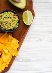 Guacamole with corn nachos, lime, cut half avocado on wooden board. White wooden surface. Top view. Space for text.