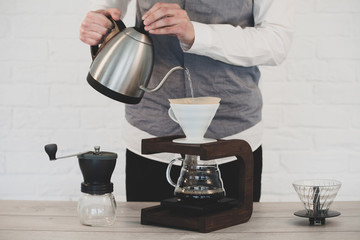 Man Making pour-over coffee with a hario V60 dripper. Coffee grinder, coffee stand and pour-over on a wooden table