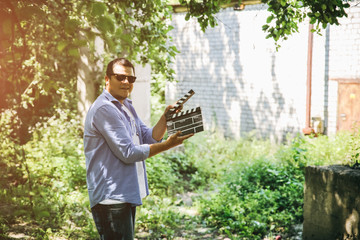 Cool hipster guy is holding in his hands a black clapperboard . Man is directing and filming some...