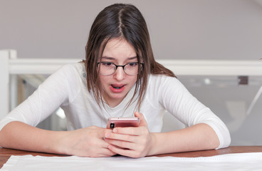 Cute tween girl looking at smartphone in her hands with scared shocked and surprised face expression. Child and gadget concept. Internet and social networks safety. Bulling