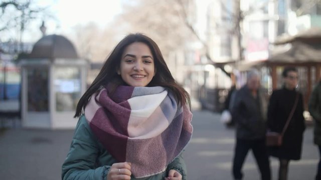 Merry young woman in modish clothes going along a street in winter in slow motion   