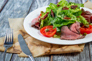 Salad leaves with sliced roast beef and sun-dried cherry tomatoes on wooden background