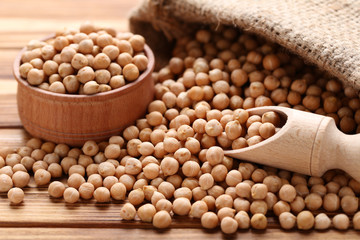 Chickpeas in bowl and sackcloth on brown wooden table