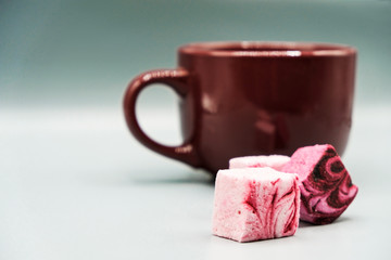 Three pieces of fruit marshmallow and a mug with a drink on a blurry background