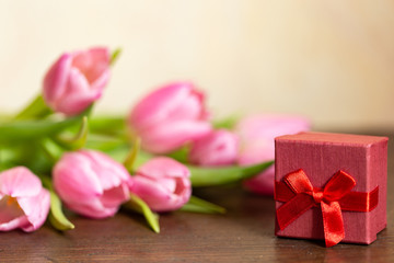 Tulpen auf Holztisch vor beigen Hintergrund rotem geschenk