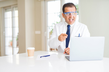 Middle age scientist man wearing professional glasses working using laptop very happy pointing with hand and finger