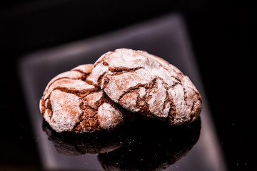 chocolate cookies with crumbs and icing sugar are laid on a black background