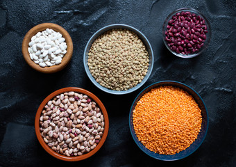 Assortment of legumes: beans and lentils. Raw healthy food. Vegetable protein. Dark background. Top view. Space for text
