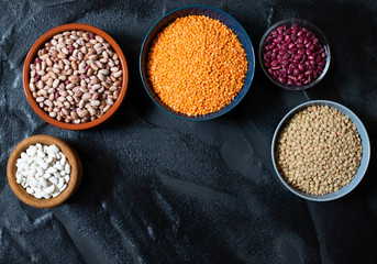 Assortment of legumes: beans and lentils. Raw healthy food. Vegetable protein. Dark background. Top view. Space for text