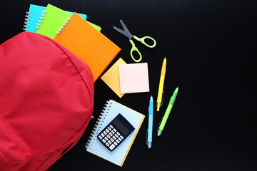Red backpack with school supplies on black background