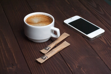 Smartphone with notebook and cup of strong coffee on wooden background
