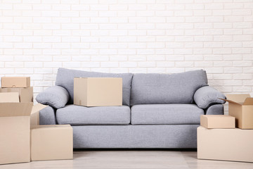 Fototapeta na wymiar Cardboard boxes with grey sofa on brick wall background