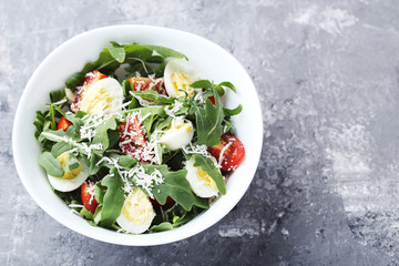 Salad with arugula leafs, tomatoes and eggs on grey wooden table