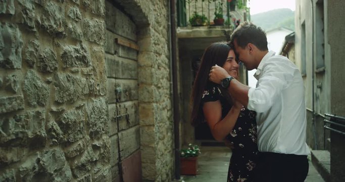 Charismatic young couple with a large smile have a romantic time in the middle off a small old street in Italy , they spending a lovely time together hugging each other. 4k