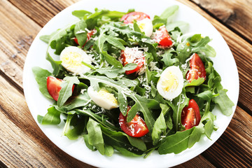 Salad with arugula leafs, tomatoes and eggs on brown wooden table