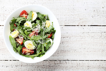 Salad with arugula leafs, tomatoes and eggs on wooden table