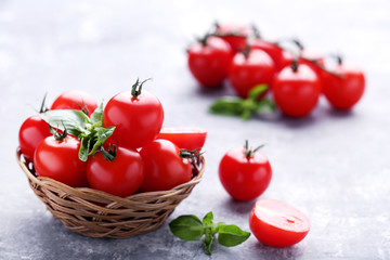 Cherry tomatoes in basket with basil leafs on grey wooden table