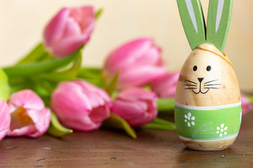 bemalter Osterhase auf tisch mit rosa tulpen