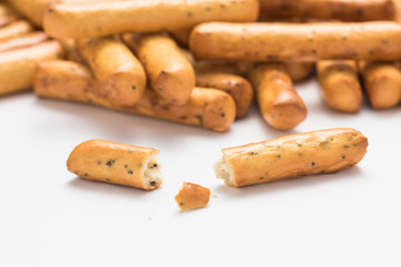 A bunch of crispy breadsticks with poppy seeds with a broken stick in the foreground.