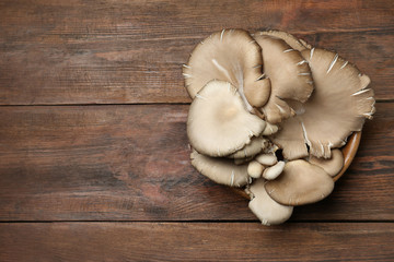 Bowl of delicious organic oyster mushrooms on wooden background, top view with space for text