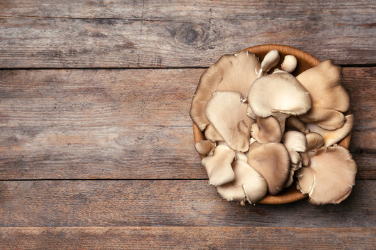 Bowl of delicious organic oyster mushrooms on wooden background, top view with space for text