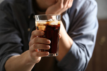 Man with glass of cold cola indoors, closeup