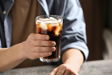 Man with glass of cold cola at table indoors, closeup