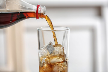 Pouring cola from bottle into glass on blurred background, closeup