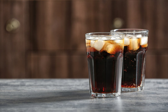 Glasses of cold cola on table against blurred background. Space for text
