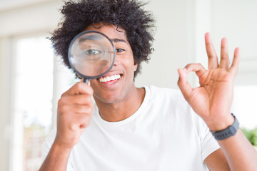 African American man looking through magnifying glass doing ok sign with fingers, excellent symbol