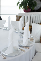 closeup white napkins stand in  white plates on served table in the restaurant. clean white dishes layout on a white tablecloth