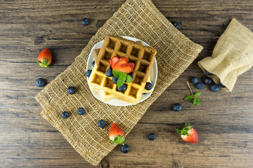delicious homemade Belgian soft waffles with fresh raspberry, blueberry, fruit, berries and whipped cream side view, selective focus on natural wooden background in rustic style