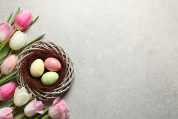 Flat lay composition with painted Easter eggs in wicker nest and tulips on color background, space for text