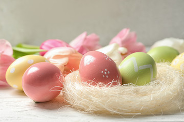 Sisal nest and painted Easter eggs on wooden table, closeup