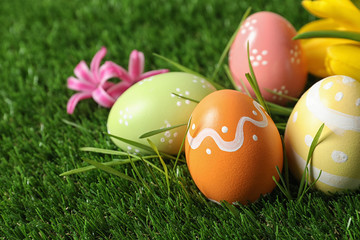 Fototapeta na wymiar Colorful painted Easter eggs and flowers on green grass, closeup. Space for text