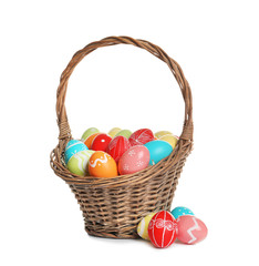 Wicker basket with painted Easter eggs on white background