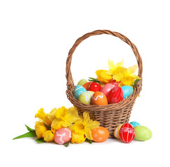 Wicker basket with painted Easter eggs and flowers on white background