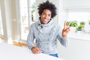 African American man wearing winter sweater smiling with happy face winking at the camera doing victory sign. Number two.