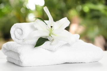 Fototapeta na wymiar Soft bath towels and flower on table against blurred background