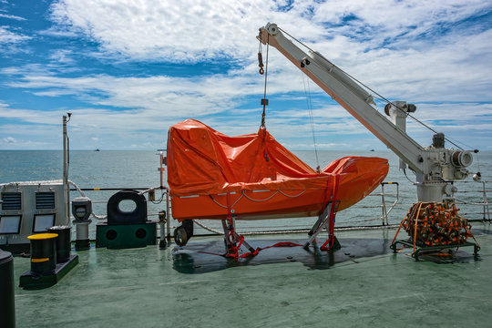 Orange lifeboat hanging on a cargo ship davit.