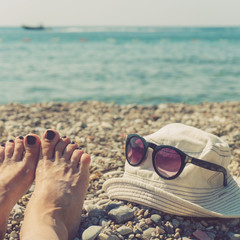 Women's feet, cap and sunglasses on the beach