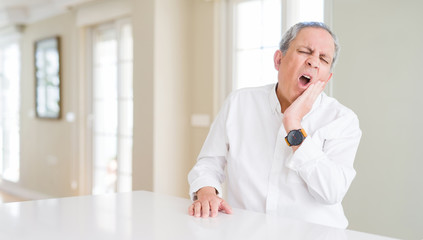 Handsome senior man at home touching mouth with hand with painful expression because of toothache or dental illness on teeth. Dentist concept.