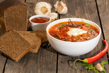 Russian borsch on a wooden table with black bread and seasonings