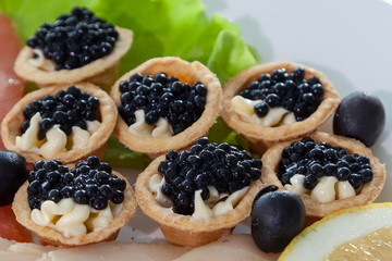 small sandwiches with black caviar and butter, a slice of lemon and lettuce