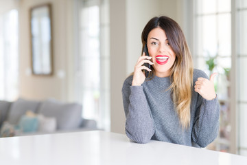 Young beautiful woman talking on the phone at home pointing and showing with thumb up to the side with happy face smiling