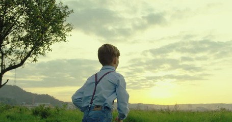 Back view of the little teen Caucasian boy playing and launching a plane toy model,then running away in the nice field lawn. Rear.